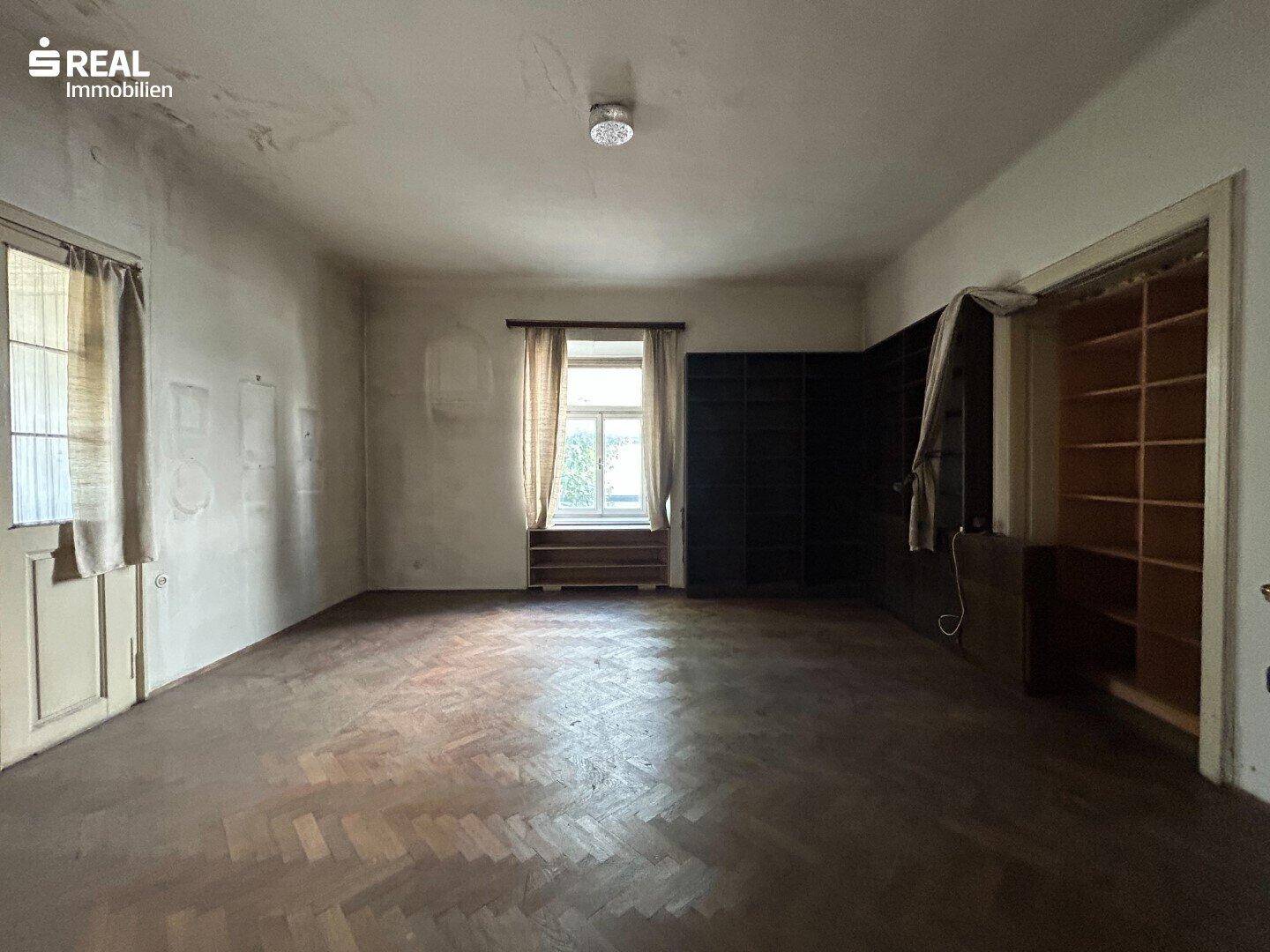 Leerer Raum mit Fischgrätparkett und eingebauten Regalen, der auf eine Renovierung wartet.