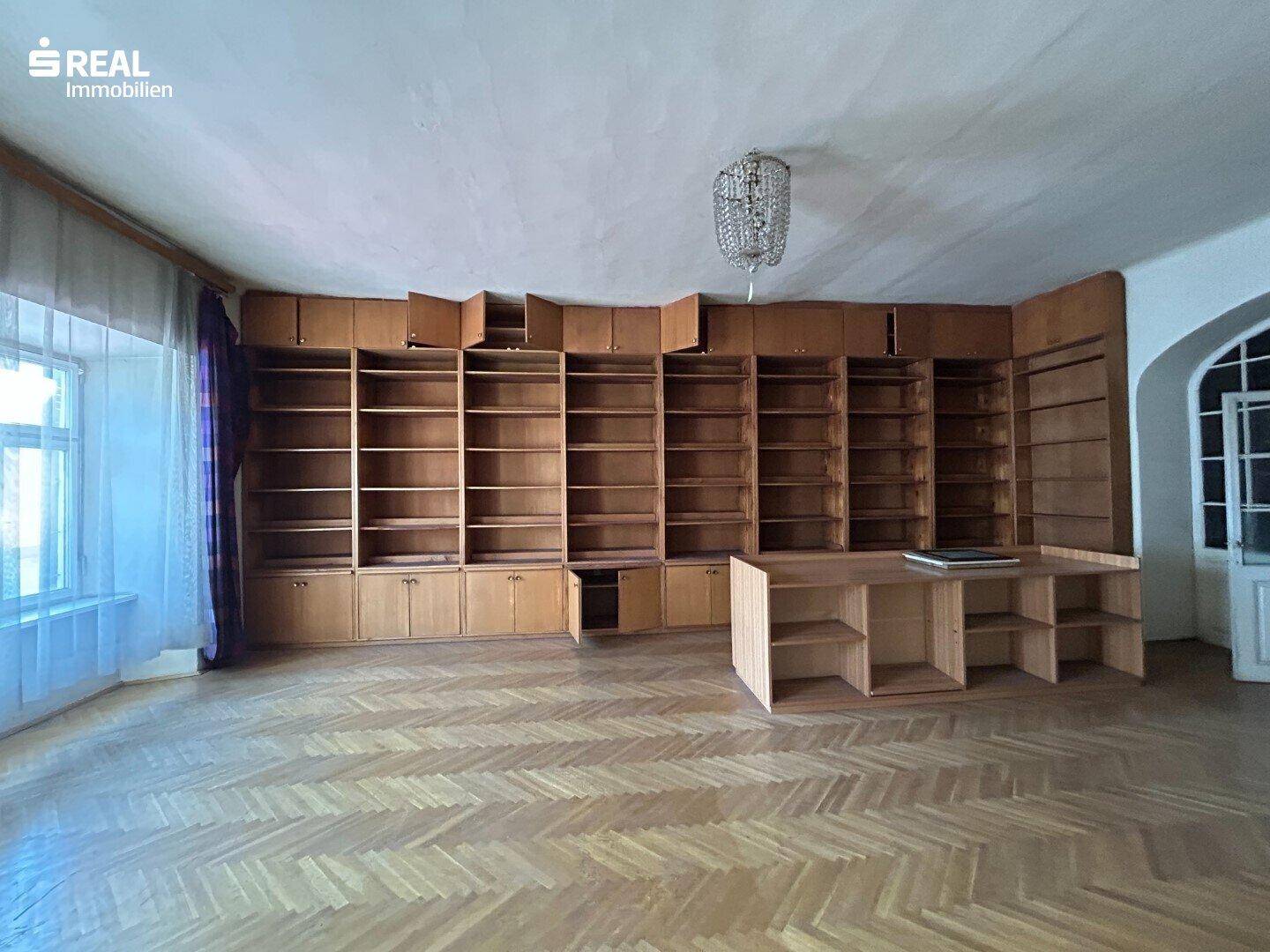 Großer Raum mit Fischgrätparkett und einer Wand voller eingebauter Holzregale, die viel Stauraum bieten.