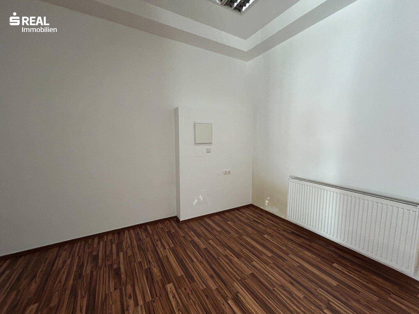 Heller Ladenraum mit Laminatboden und einem Heizkörper, ideal für ein kleines Geschäft oder Büro.