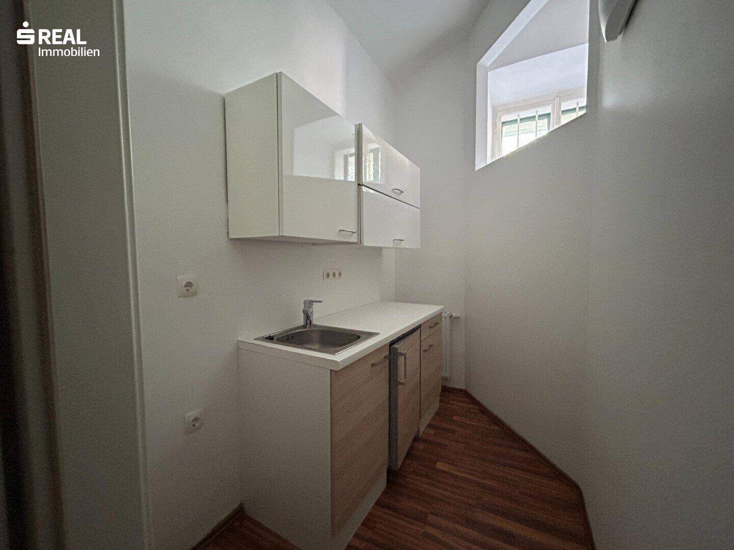 Kleine Küchenzeile mit Spüle, Unterschränken und Hängeschränken, ideal für ein Büro oder eine kleine Wohnung.