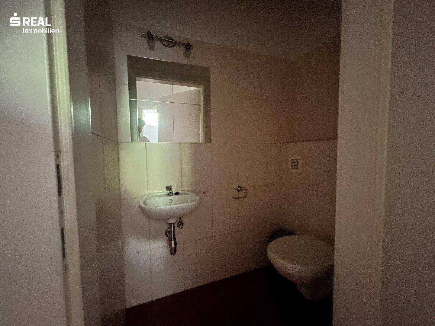 Einfache Toilette mit Waschbecken und Fliesen an den Wänden, die eine Modernisierung benötigt.