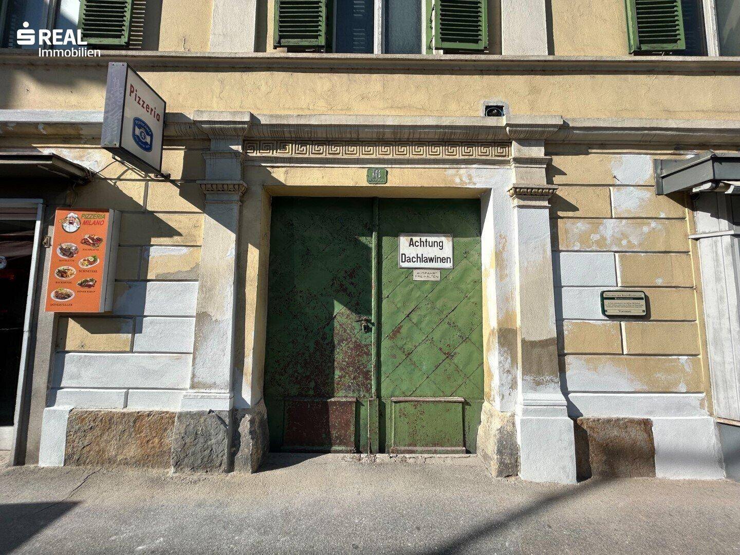 Historischer Eingang mit grünen Holztüren und einem Schild, das auf Dachlawinen hinweist.