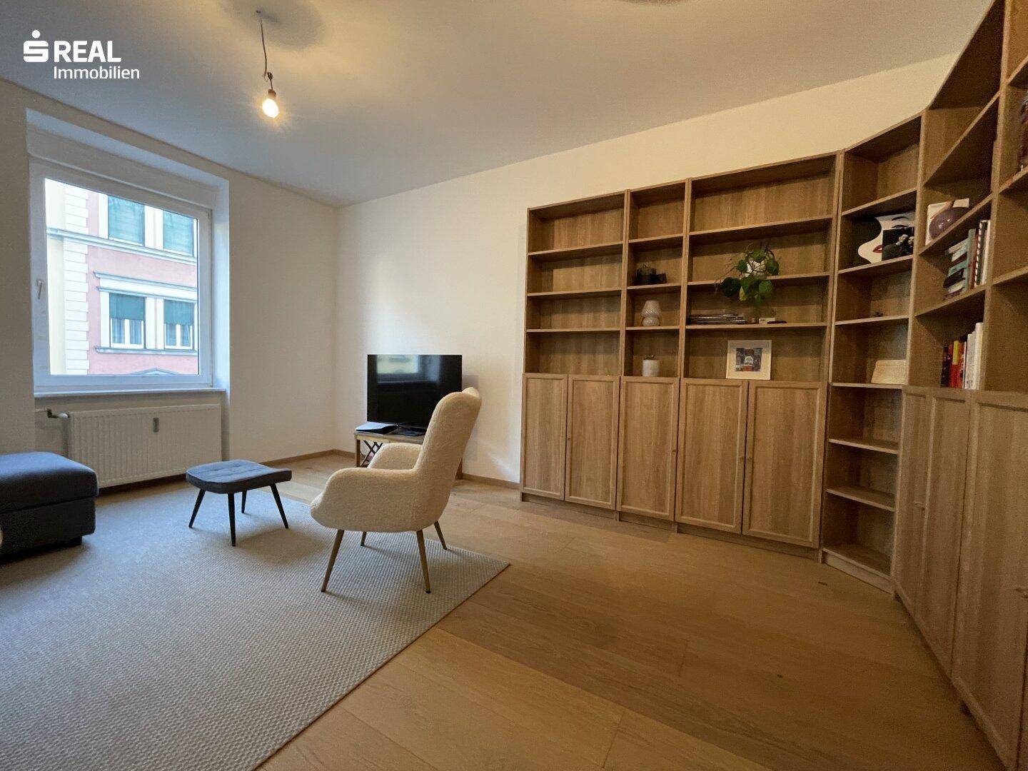 Geräumiges Wohnzimmer mit großem Holzregal, Fernseher und hellem Sessel.
