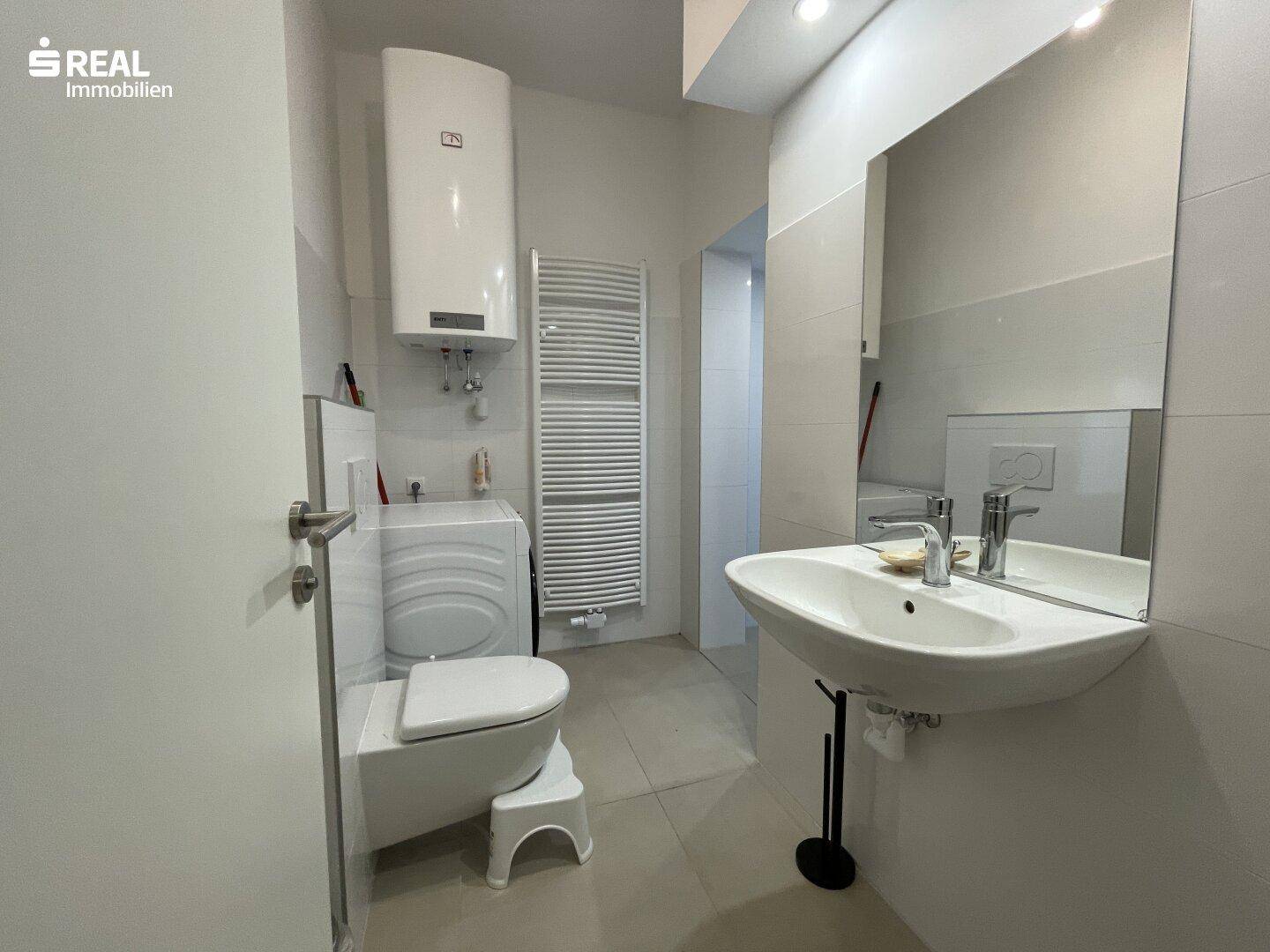 Modernes Badezimmer mit WC, Waschbecken, Spiegel und Waschmaschine.