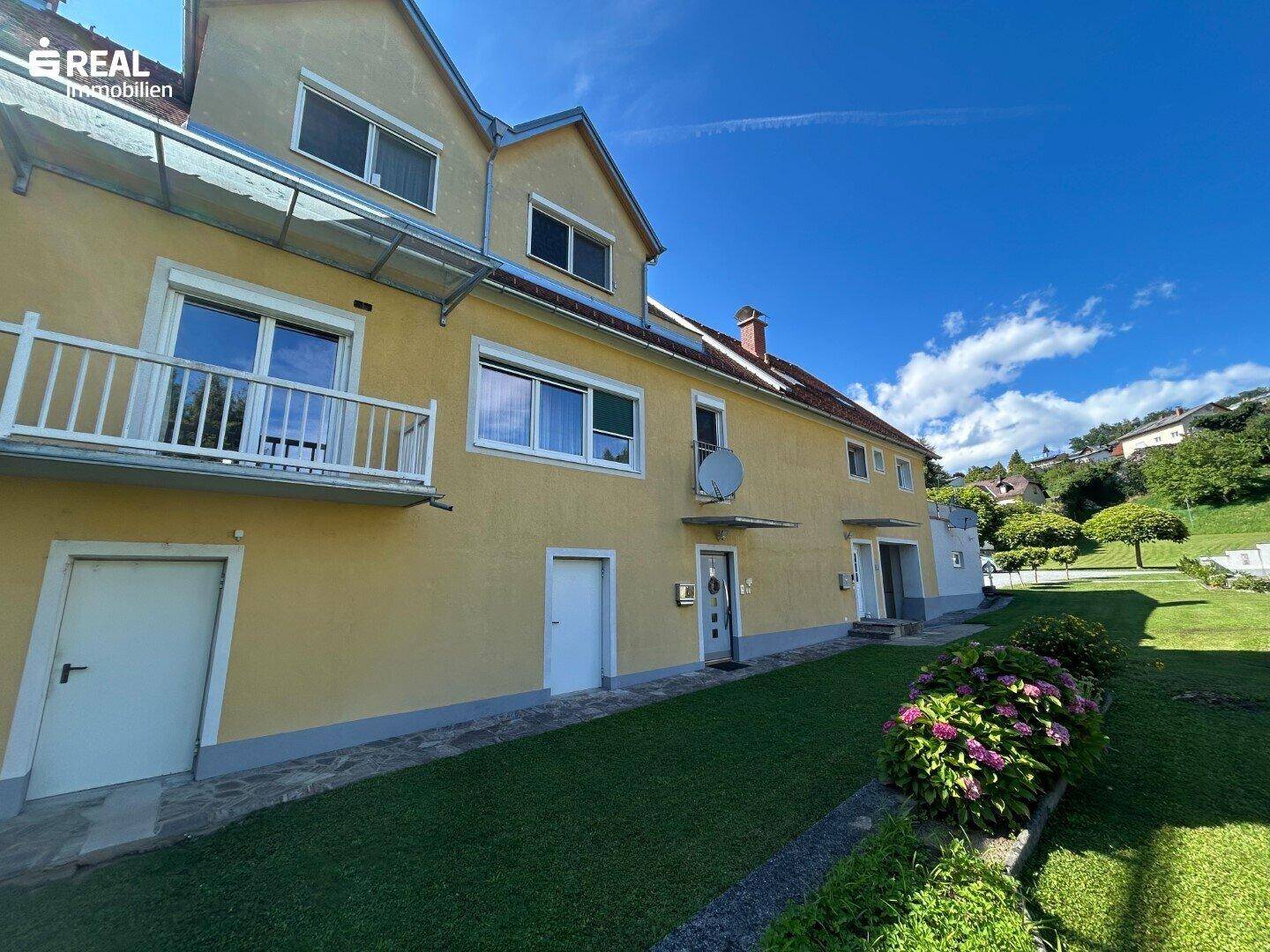 Seitenansicht des Hauses mit gepflegtem Rasen, blühenden Büschen und sonnigem Garten.