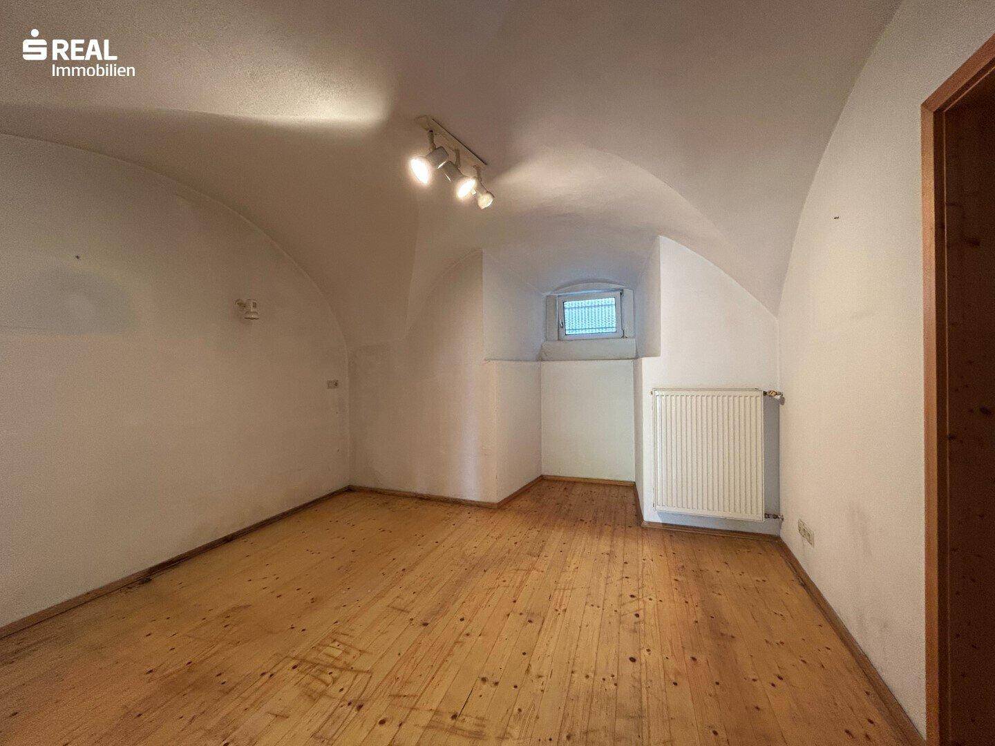 Leerer Raum mit Holzboden, gewölbter Decke und kleinem Fenster, bereit zur Gestaltung.