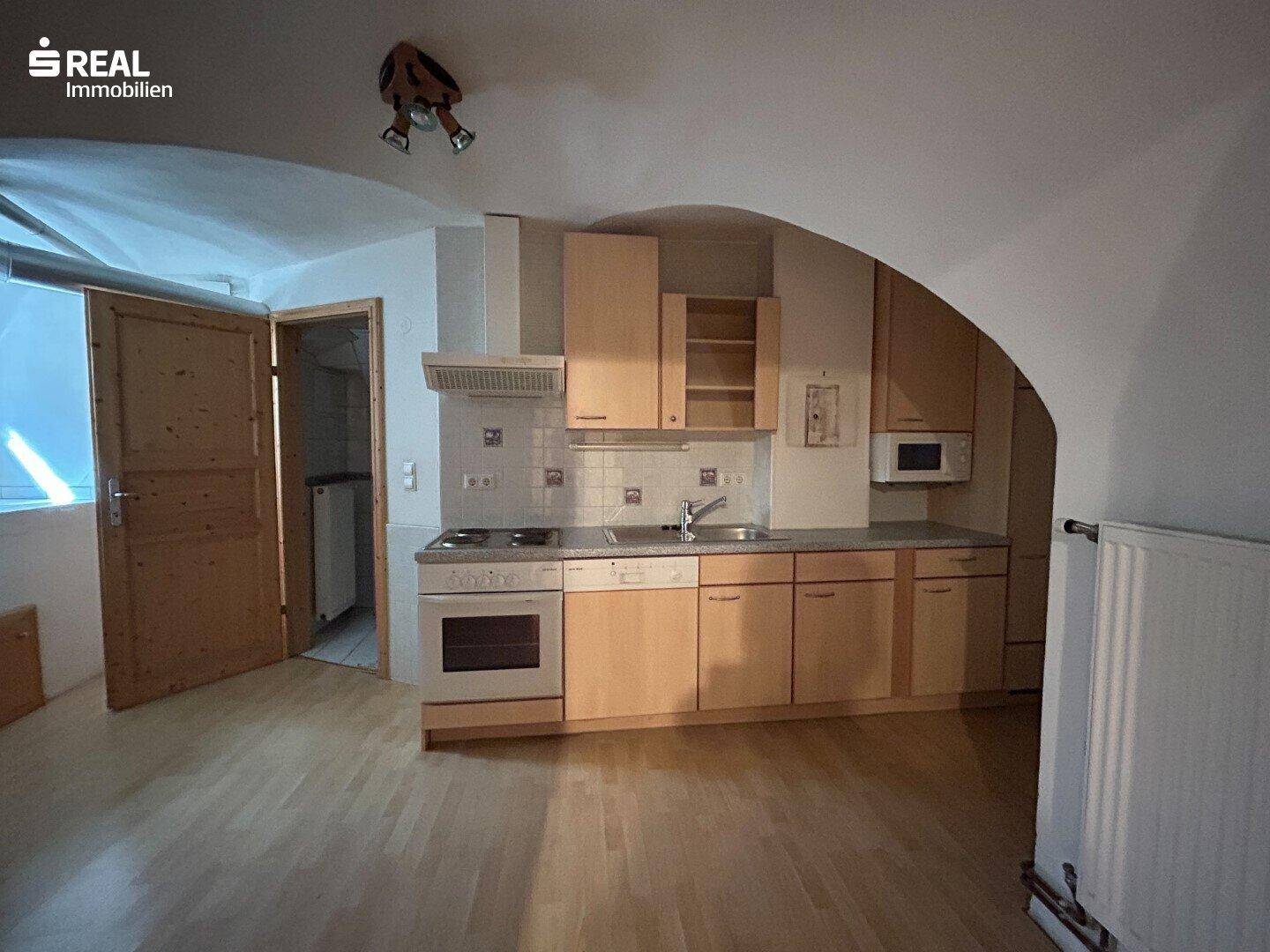Kleine Küche mit hellen Holzschränken, Einbaugeräten und gewölbter Decke.