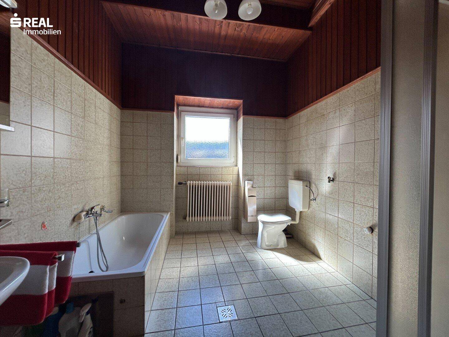 Badezimmer mit Badewanne, Dusche und WC, ausgestattet mit hellen Fliesen und Fenster.