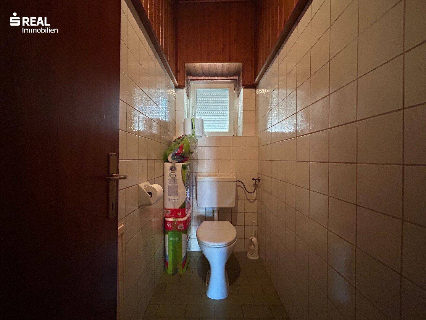 Separate Gästetoilette mit Fenster und hellen Fliesen, praktisch und einfach gehalten.