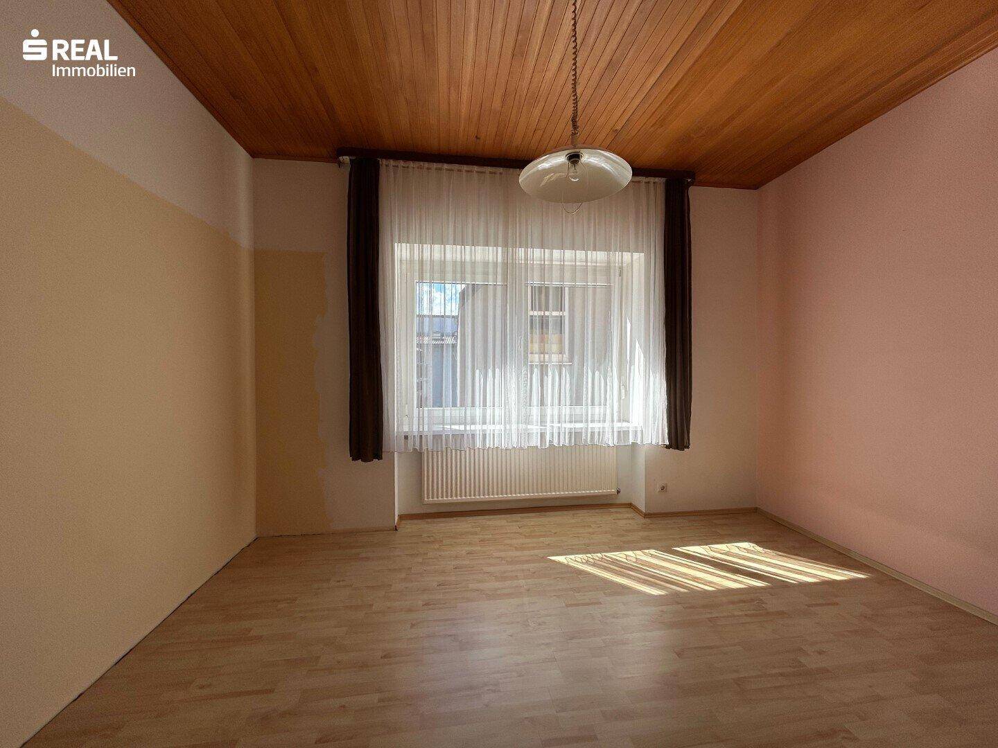 Heller Raum mit Laminatboden, Holzdecke und großem Fenster, ideal für Schlaf- oder Wohnbereich.