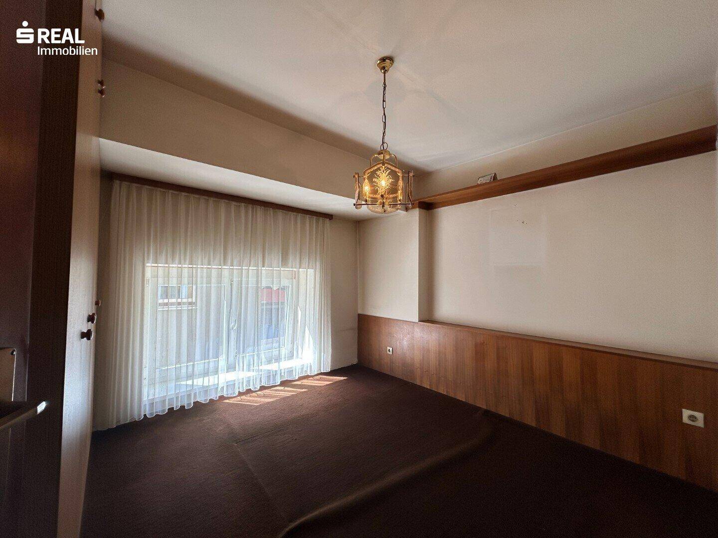 Zimmer mit Teppichboden, Holzvertäfelung und Fenster, bietet eine gemütliche Atmosphäre.