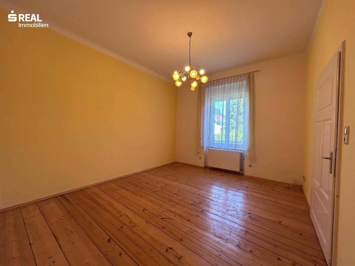 Geräumiger Raum mit Holzboden und gelben Wänden, ideal für Schlaf- oder Wohnbereich.