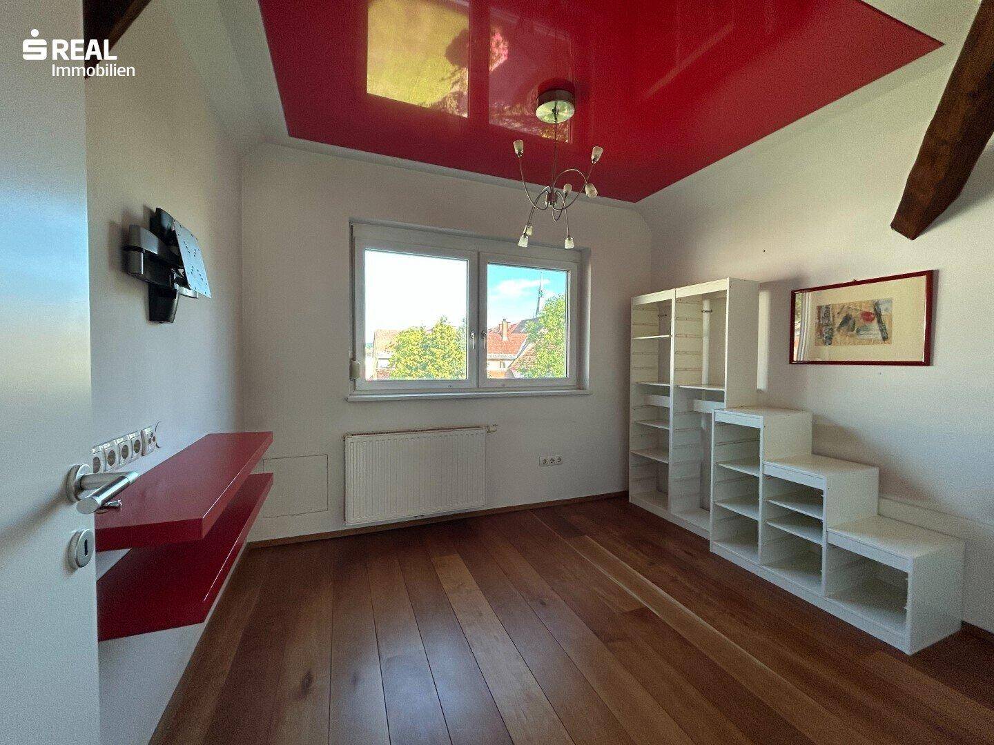 Schlafzimmer mit Holzboden, roter Decke und großem Fenster, modern eingerichtet.
