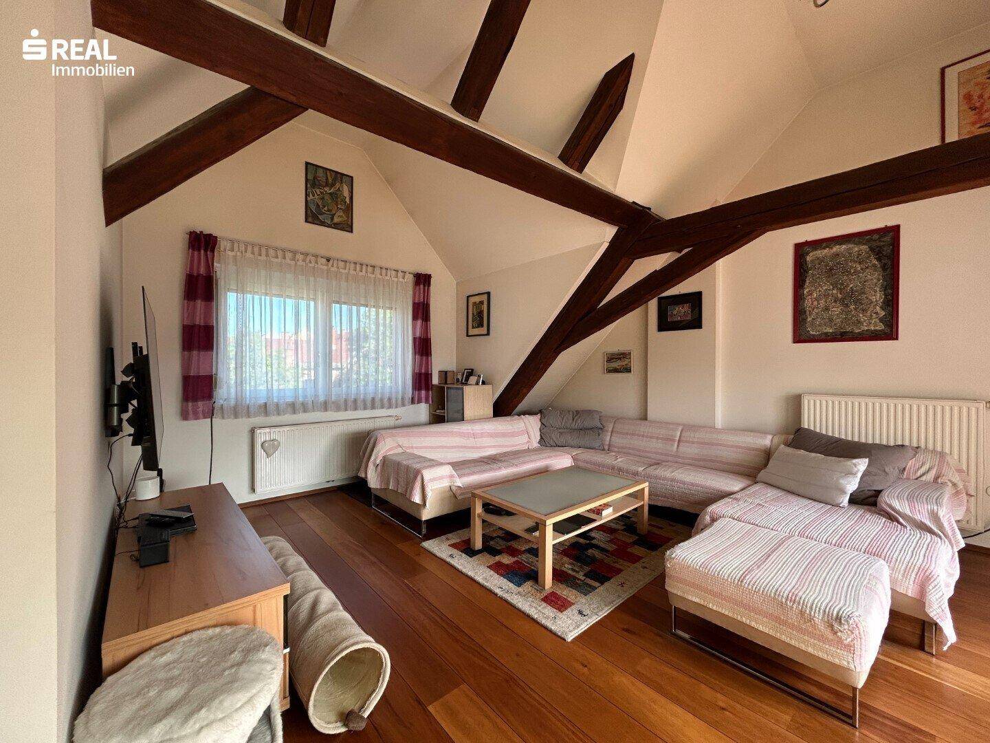 Geräumiges Wohnzimmer mit Holzboden, Holzbalken und großem Sofa, gemütlich eingerichtet.