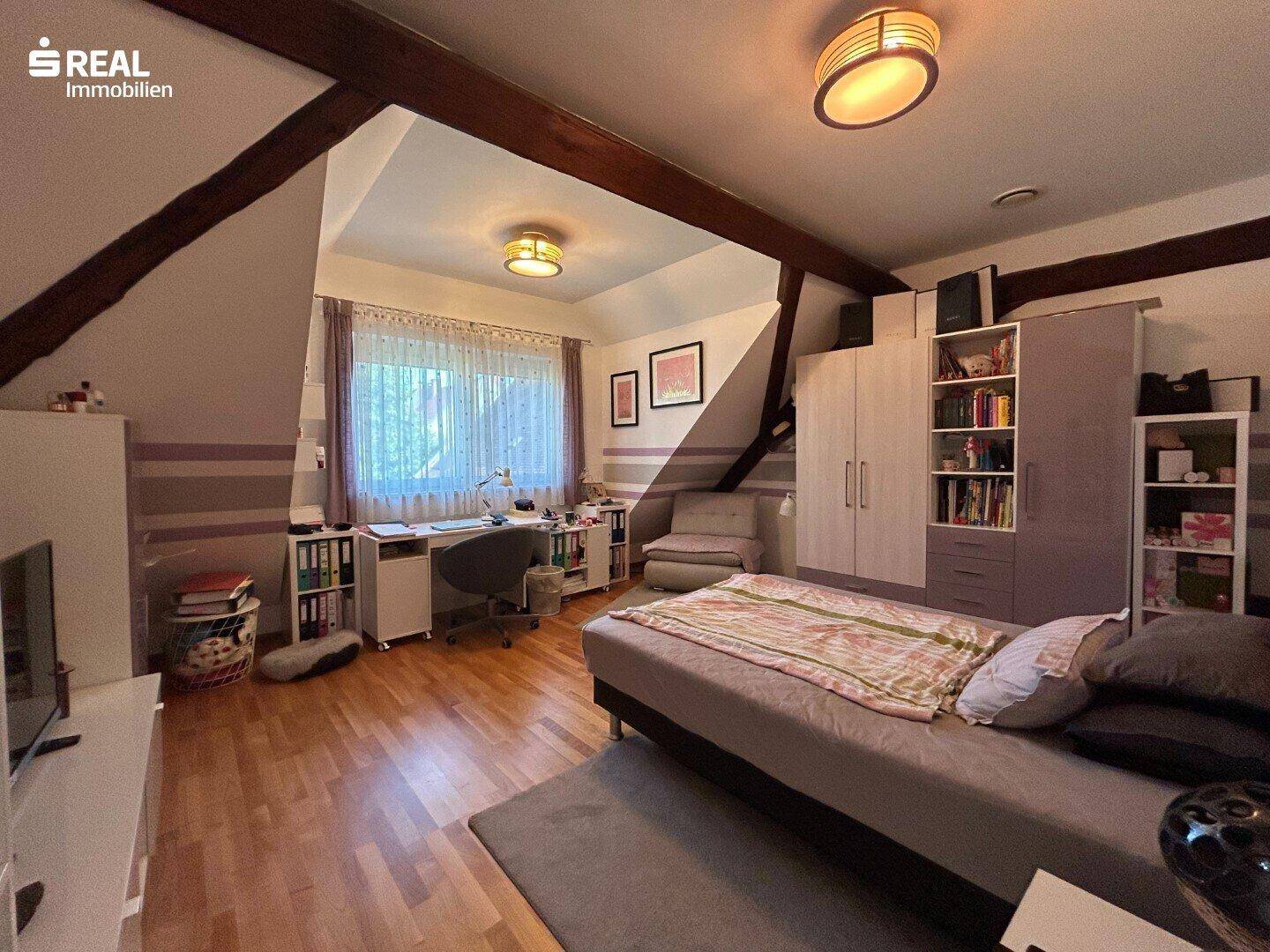 Geräumiges Schlafzimmer mit Holzboden, Dachschrägen und großem Fenster, als Büro genutzt.
