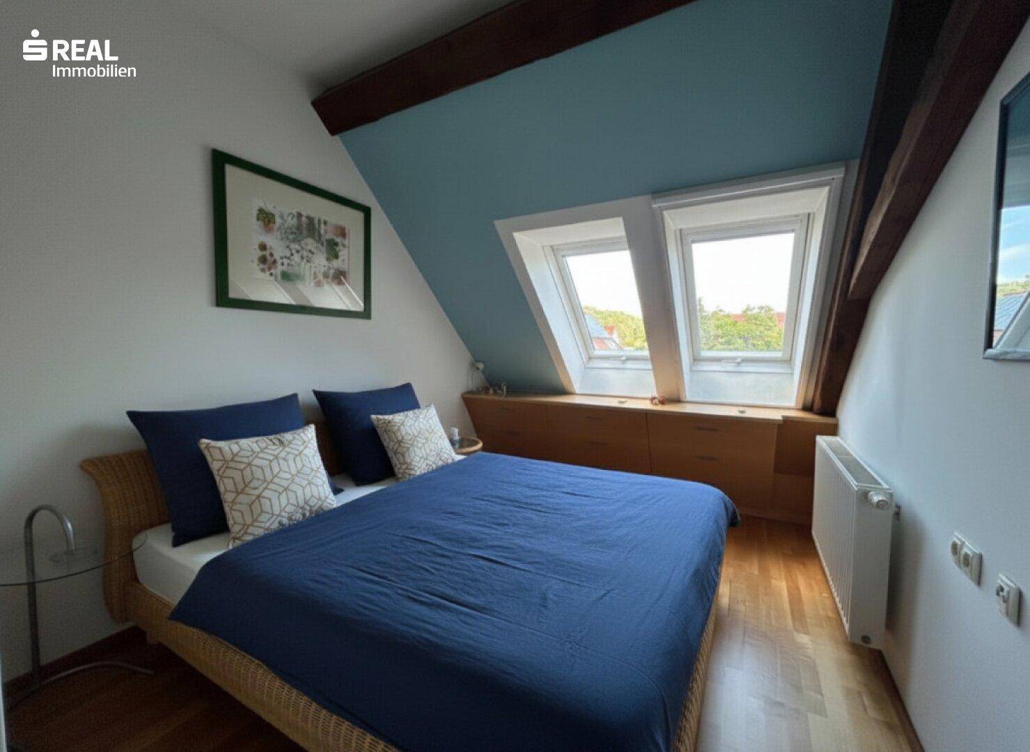 Schlafzimmer mit Holzboden, Dachschrägen und zwei Dachfenstern, hell und gemütlich.