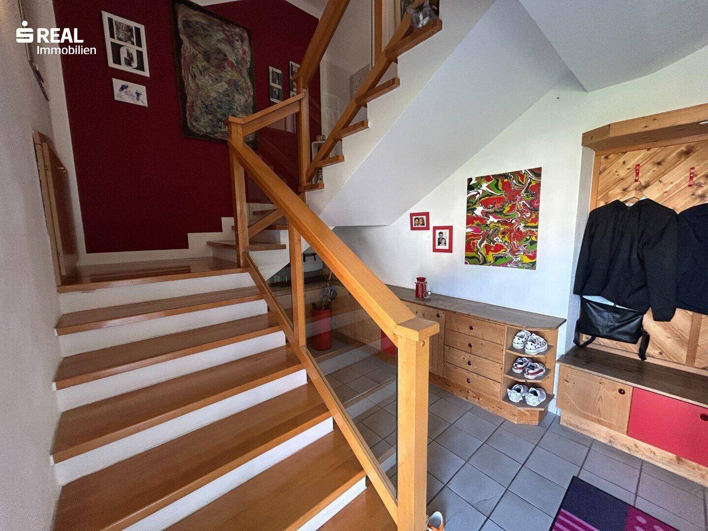 Heller Eingangsbereich mit Holztreppe und moderner Glasbrüstung, einladend gestaltet.