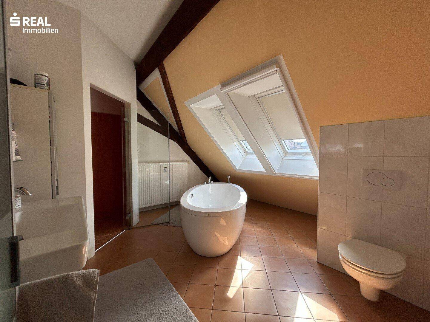 Modernes Badezimmer mit freistehender Badewanne, Dachschrägen und Dachfenstern, hell und stilvoll.
