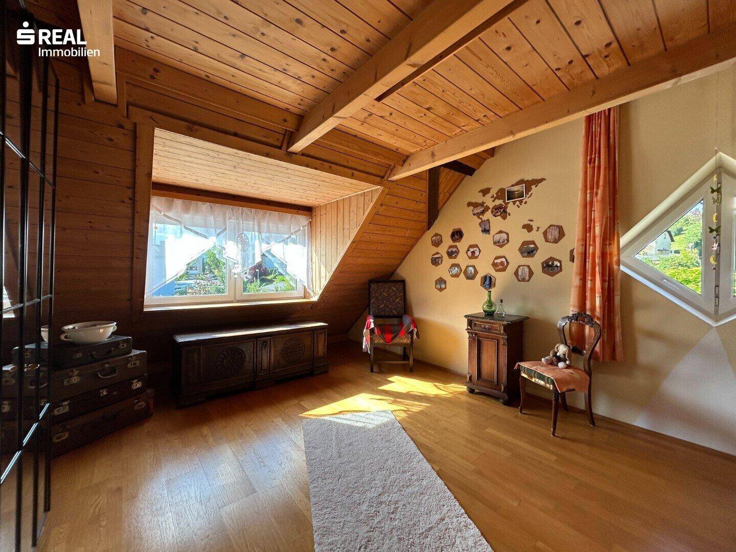 Gemütlicher Wohnbereich im Dachgeschoss mit Holzboden, Holzdecke und großem Fenster.