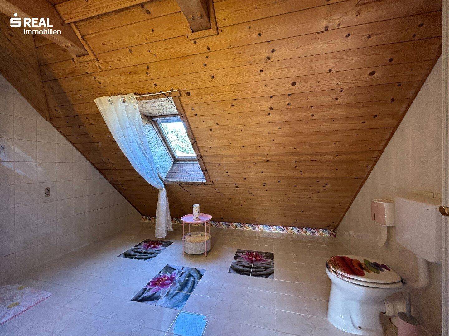 Badezimmer im Dachgeschoss mit Fliesenboden, Holzdecke und Dachfenster, funktional eingerichtet.