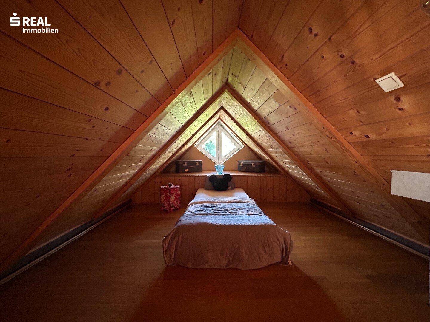 Gemütliches Schlafzimmer im Dachgeschoss mit Holzboden, Holzdecke und Giebelfenster.
