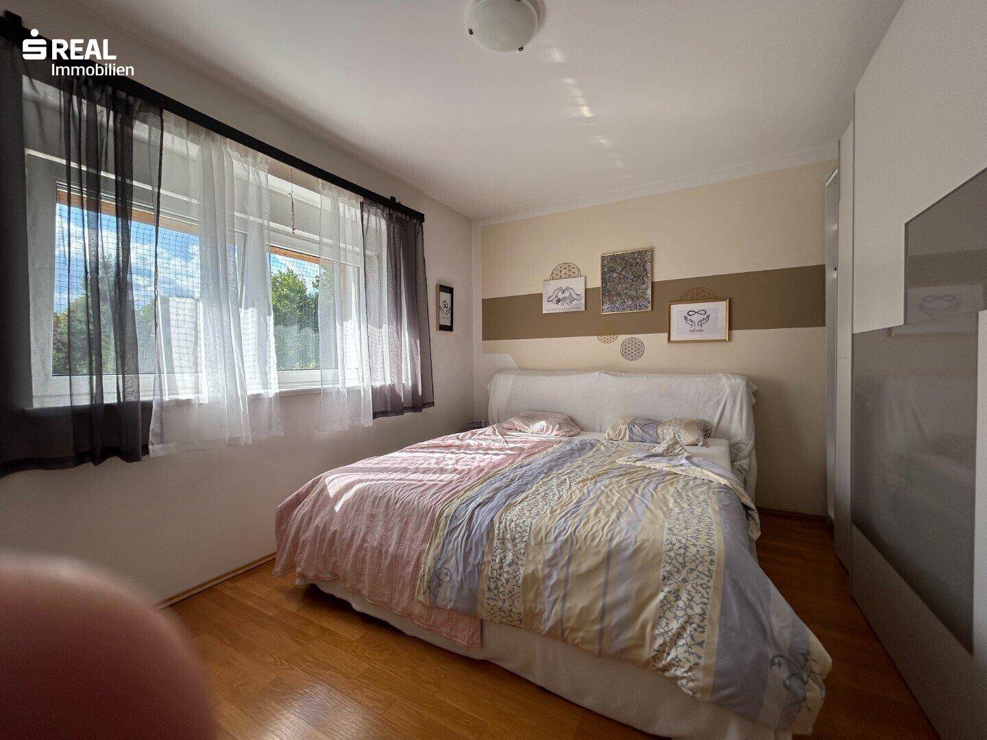 Helles Schlafzimmer mit Holzboden, großem Fenster und gemütlichem Doppelbett.