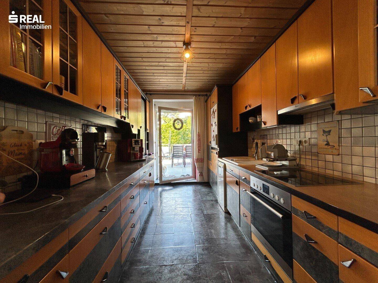 Lange Küche mit Holzschränken, Fliesenboden und Zugang zu einer Außenterrasse.