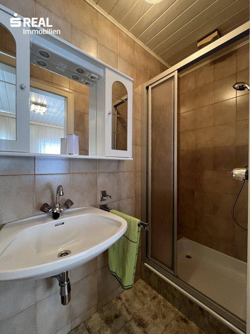 Kleines Badezimmer mit Duschkabine, Waschbecken und Spiegelschrank.
