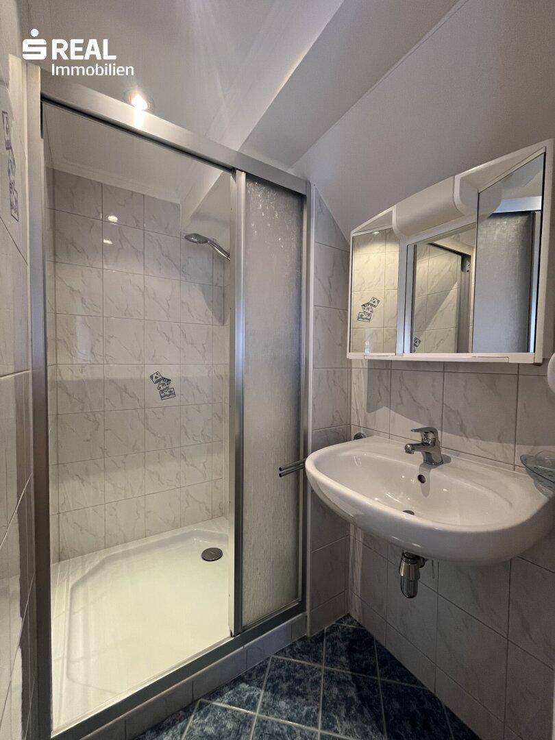 Kleines Badezimmer mit Duschkabine, Waschbecken und Fliesenboden.