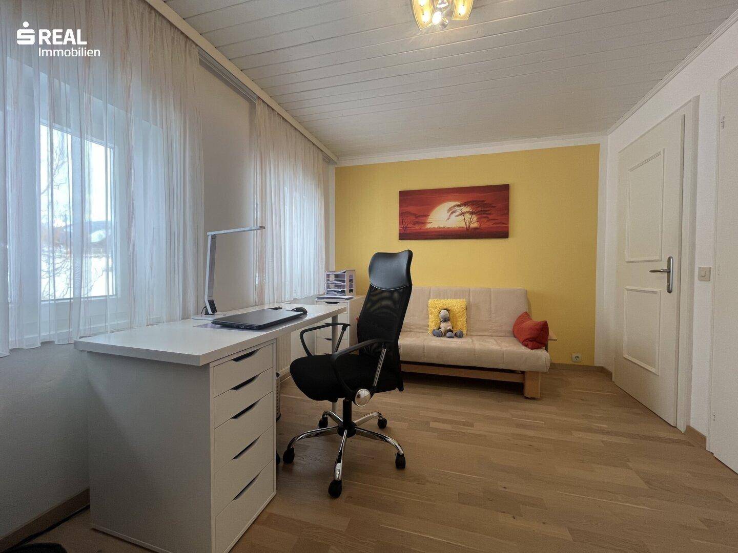 Helles Zimmer mit Schreibtisch, Sofa und Holzboden, ideal als Büro oder Gästezimmer.