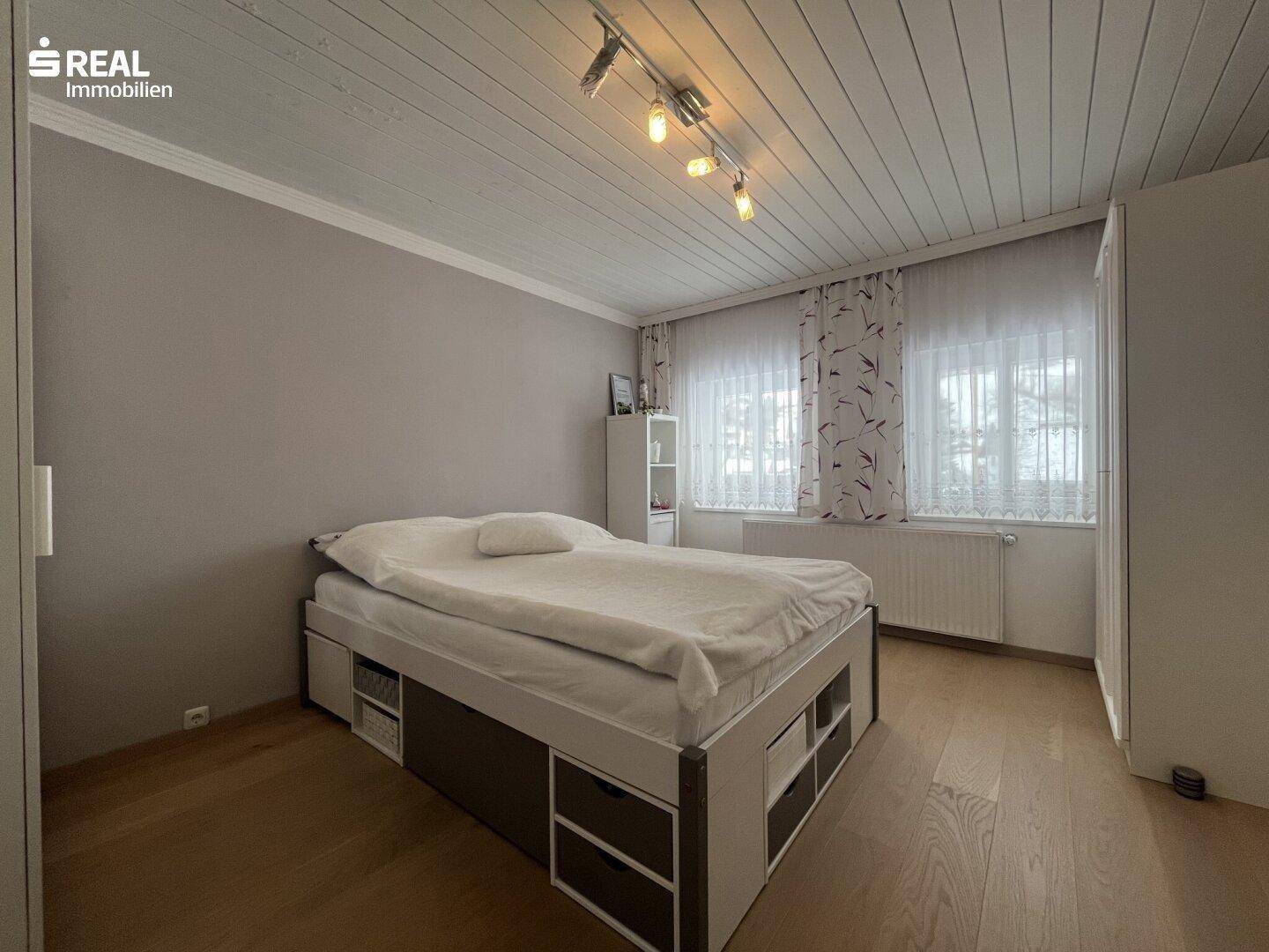 Helles Schlafzimmer mit großem Bett, Kleiderschrank und zwei Fenstern.