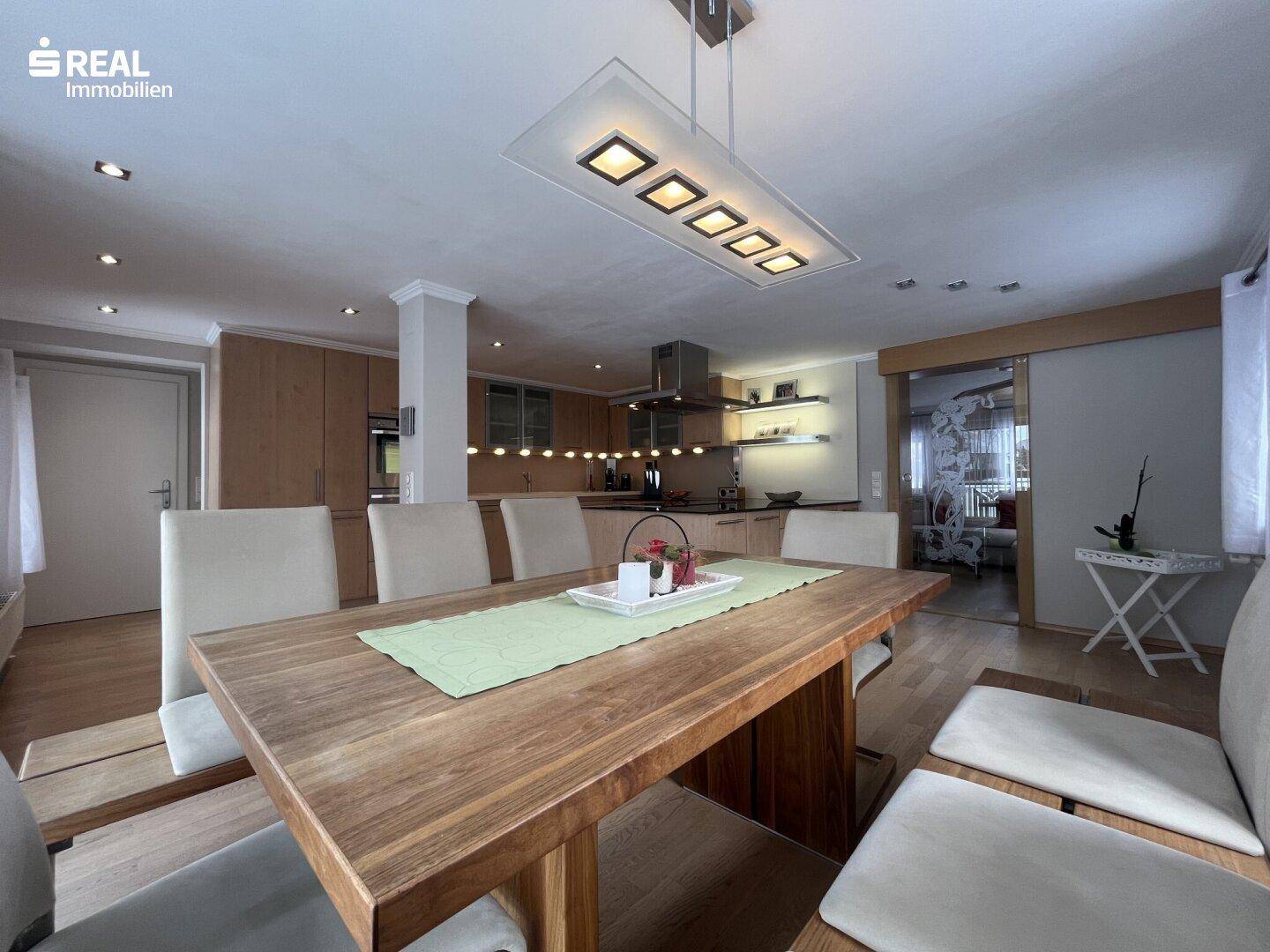 Offener Wohn- und Essbereich mit Holztisch und moderner Küche im Hintergrund.