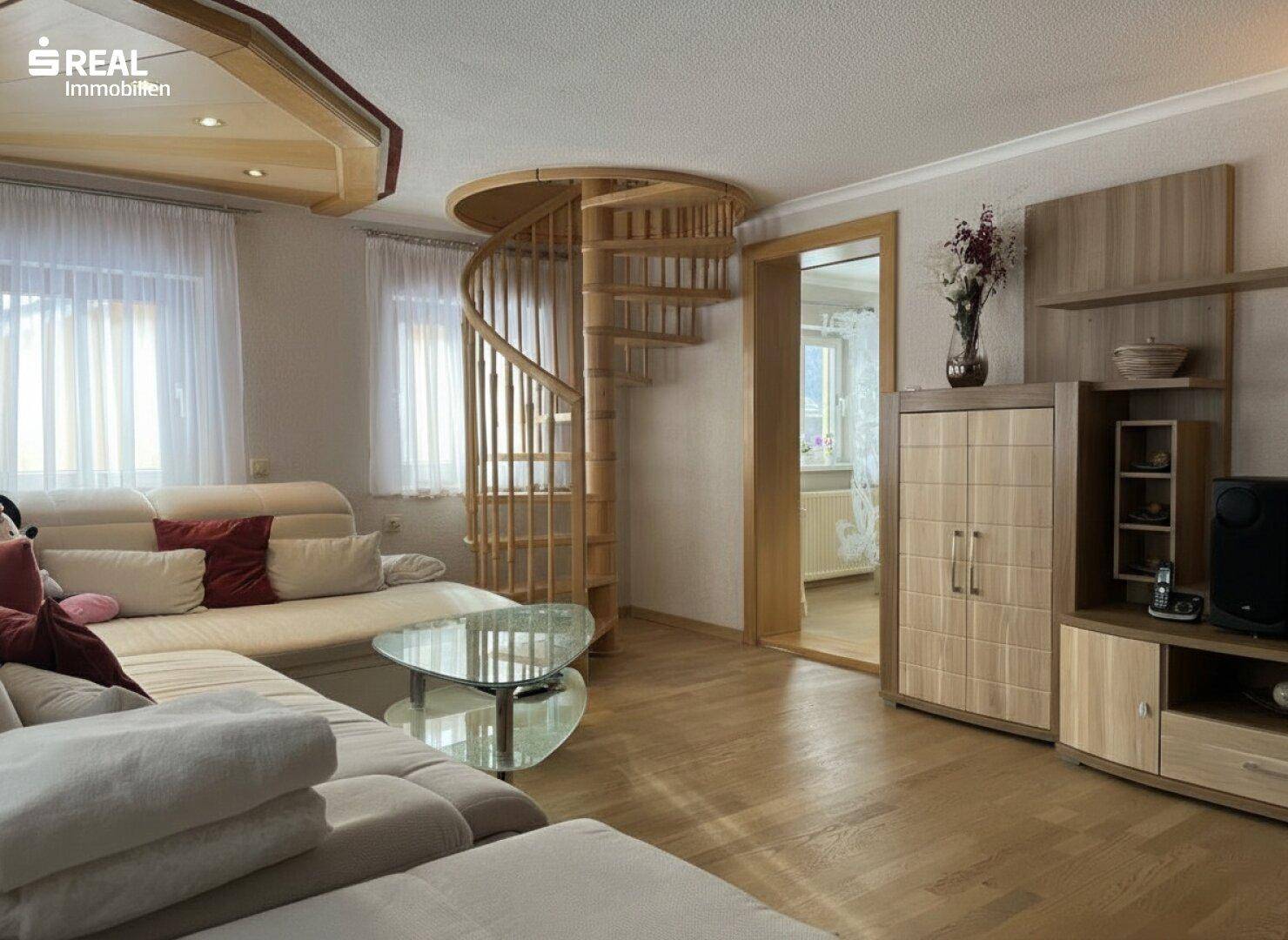 Gemütliches Wohnzimmer mit Ecksofa, Holztreppe und hellem Parkettboden.