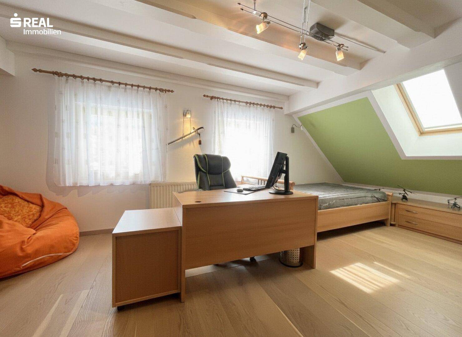 Helles Arbeitszimmer im Dachgeschoss mit Schreibtisch, Bett und Dachfenster.