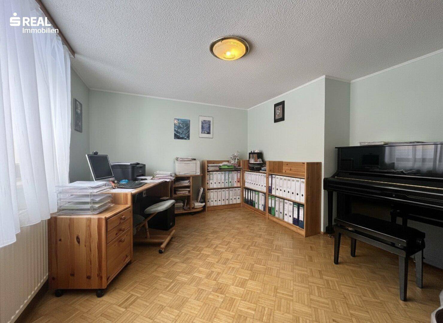 Helles Büro mit Schreibtisch, Bücherregalen und Klavier, bietet eine ruhige Arbeitsatmosphäre.