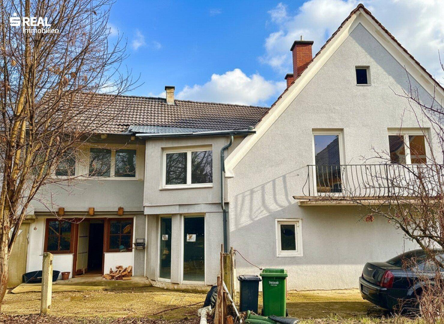 Rückansicht eines grauen Hauses mit mehreren Fenstern und einem kleinen Balkon im Obergeschoss.