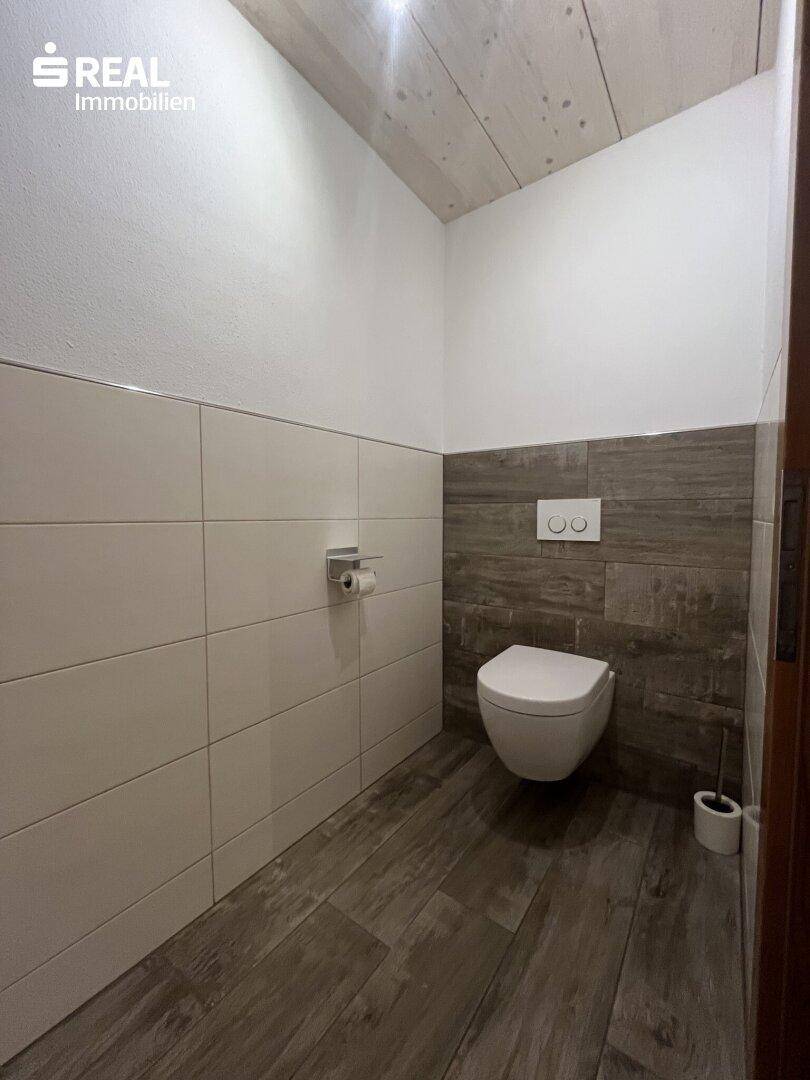 Gäste-WC mit wandhängender Toilette und modernen Fliesen in Grau- und Weißtönen.