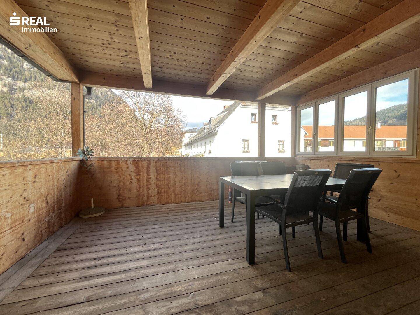 Überdachte Holzterrasse mit Esstisch und Stühlen, bietet einen weiten Blick auf die Berge.