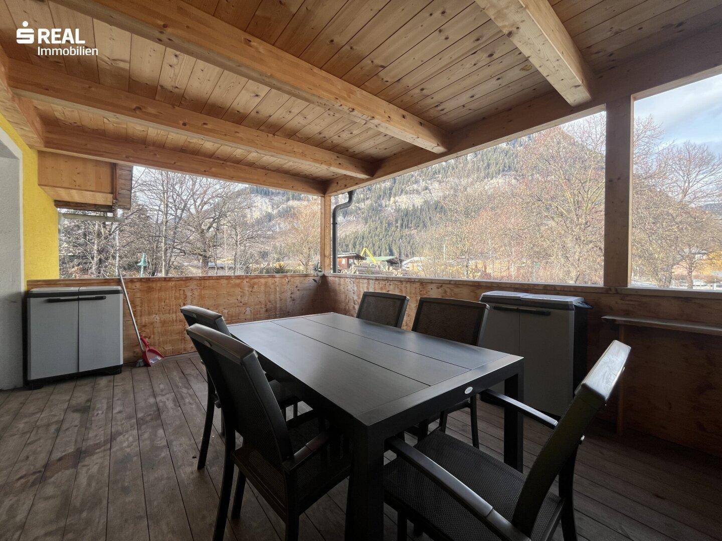 Geräumige überdachte Holzterrasse mit Esstisch und Stauraum, umgeben von Bergblick.