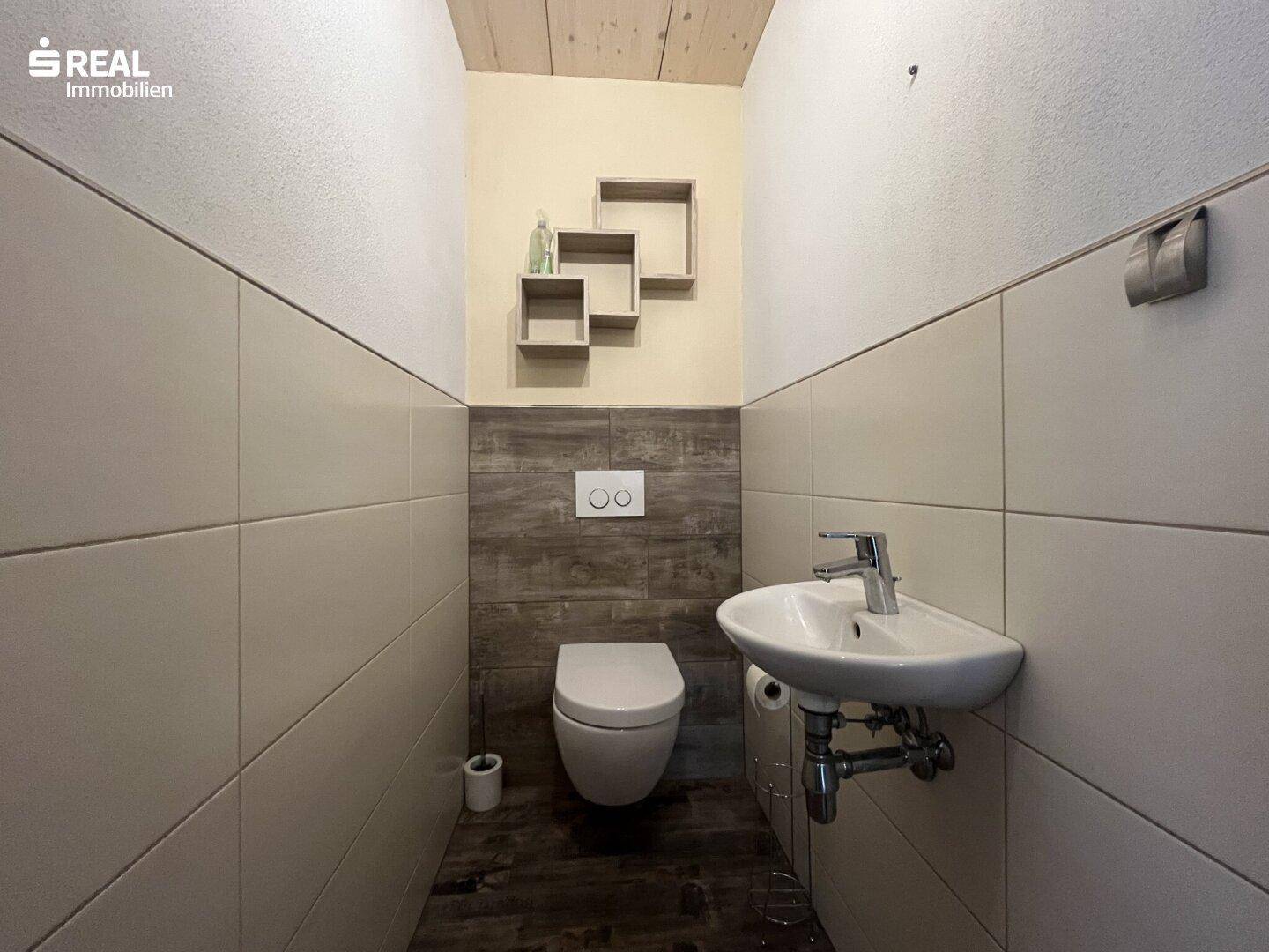 Gäste-WC mit wandhängender Toilette, kleinem Waschbecken und modernen Fliesen.
