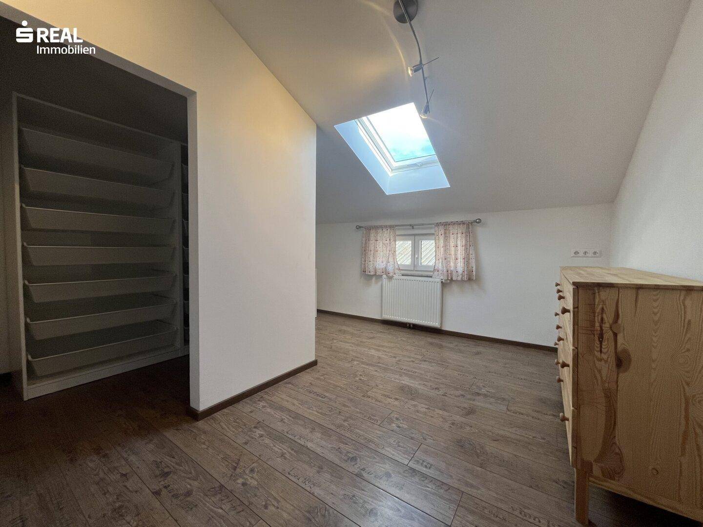 Heller Raum mit Dachfenster, Holzboden und integrierten Regalen für Stauraum.