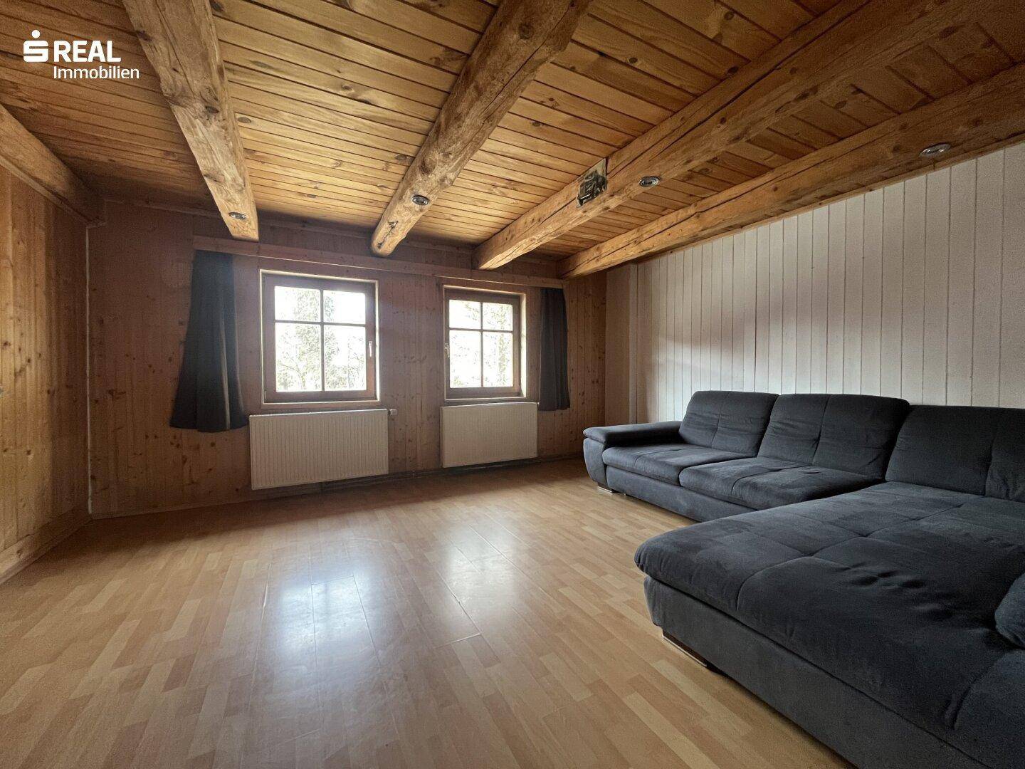 Gemütliches Wohnzimmer mit Holzwänden, Holzbalkendecke und großem Sofa.