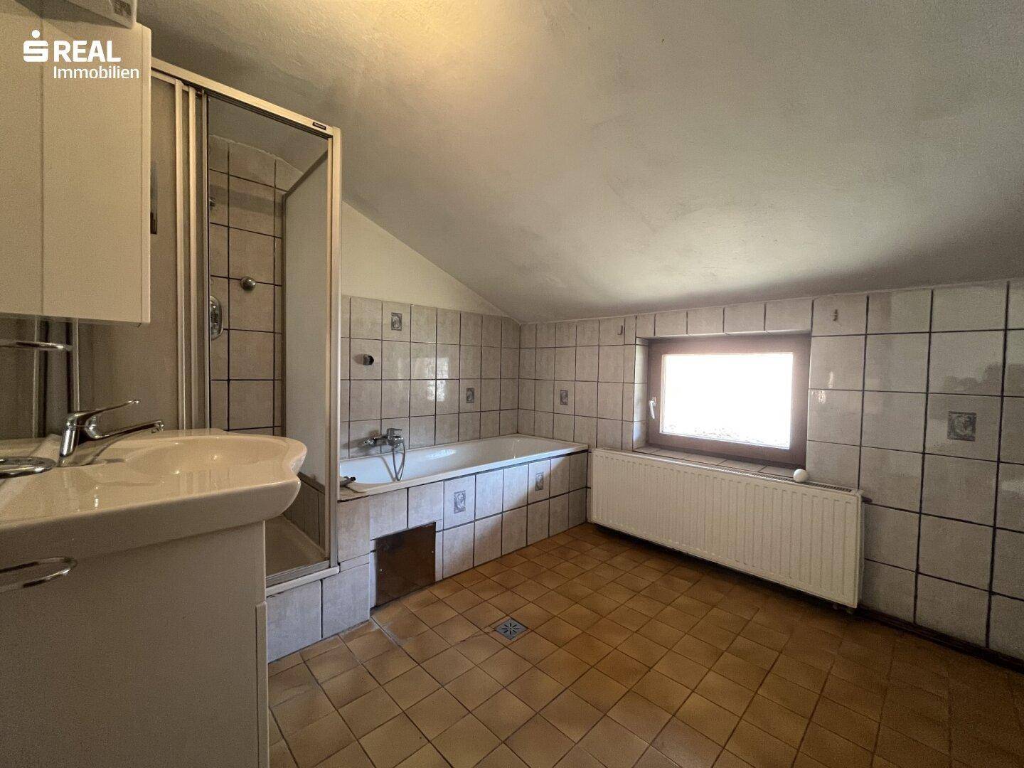 Badezimmer mit Dusche, Badewanne, Waschbecken und hellen Fliesen an Wänden und Boden.