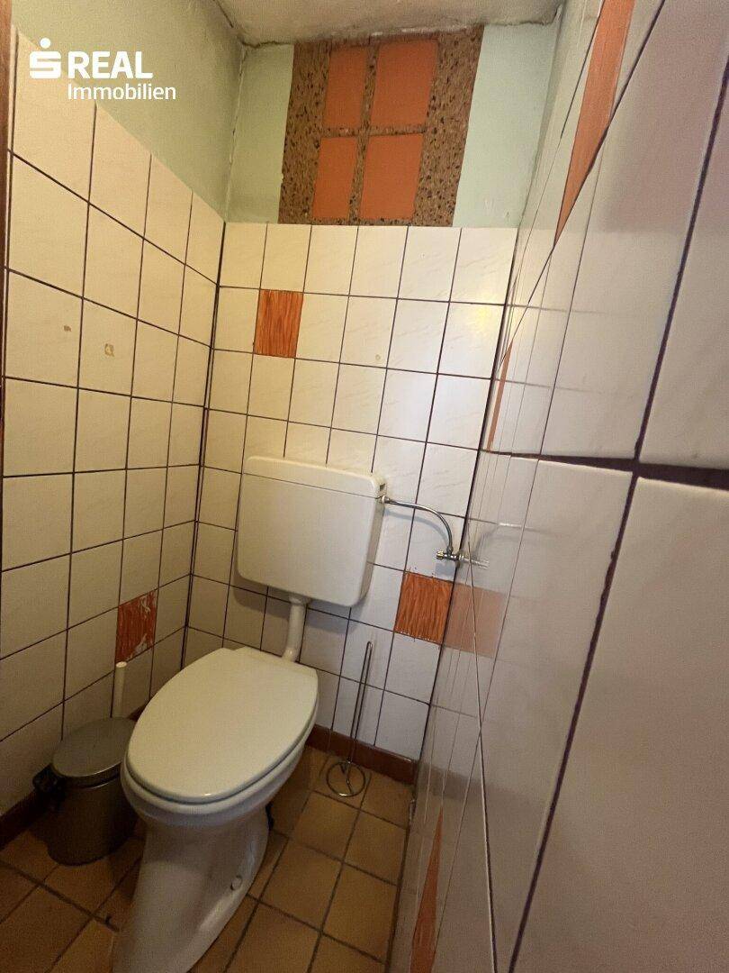 Kleines WC mit Toilette und hellen Fliesen an den Wänden, in einem älteren Stil.