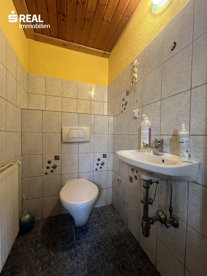 WC mit Toilette, Waschbecken und gefliesten Wänden in einem älteren, farbenfrohen Stil.