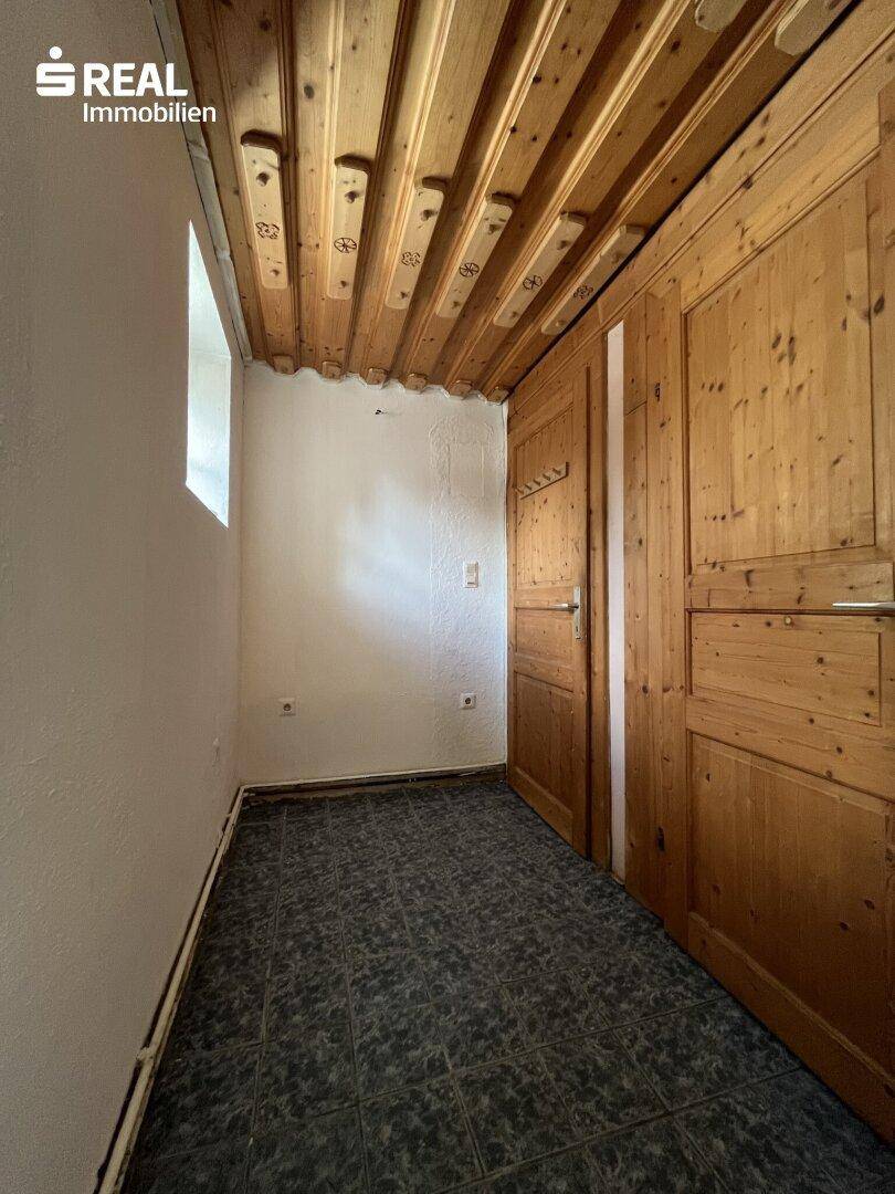 Kleiner Raum mit dunklem Fliesenboden, Holzdecke und Holztüren, möglicherweise ein Abstellraum.
