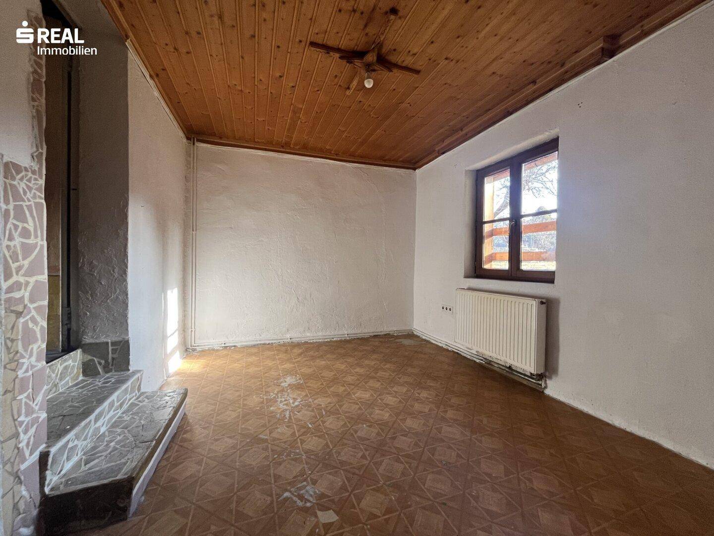 Raum mit gemustertem Linoleumboden, Holzdecke und Heizkörper unter dem Fenster.