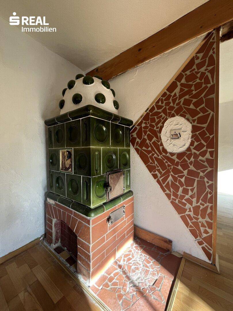 Detailansicht eines traditionellen grünen Kachelofens mit Ziegelsockel und dekorativen Fliesen.