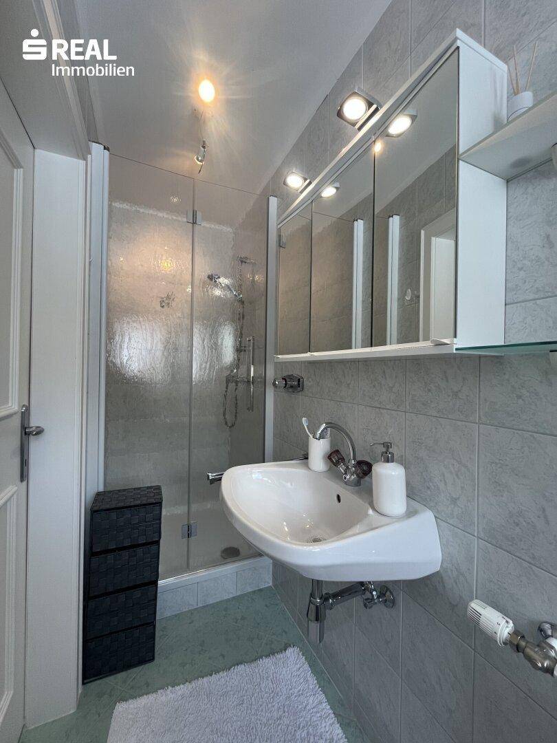 Modernes Badezimmer mit Duschkabine, Waschbecken und Spiegelschrank.