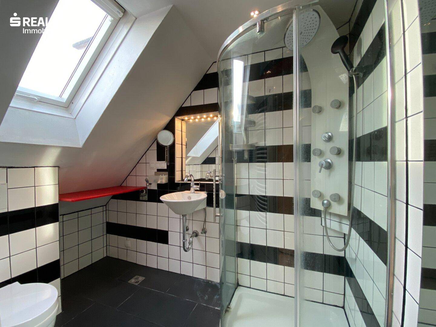 Modernes Badezimmer mit schwarz-weißen Fliesen, Dusche und Dachfenster.